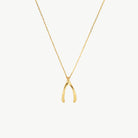 A delicate gold chain necklace featuring a small, polished gold wishbone pendant, displayed against a clean, off-white background.