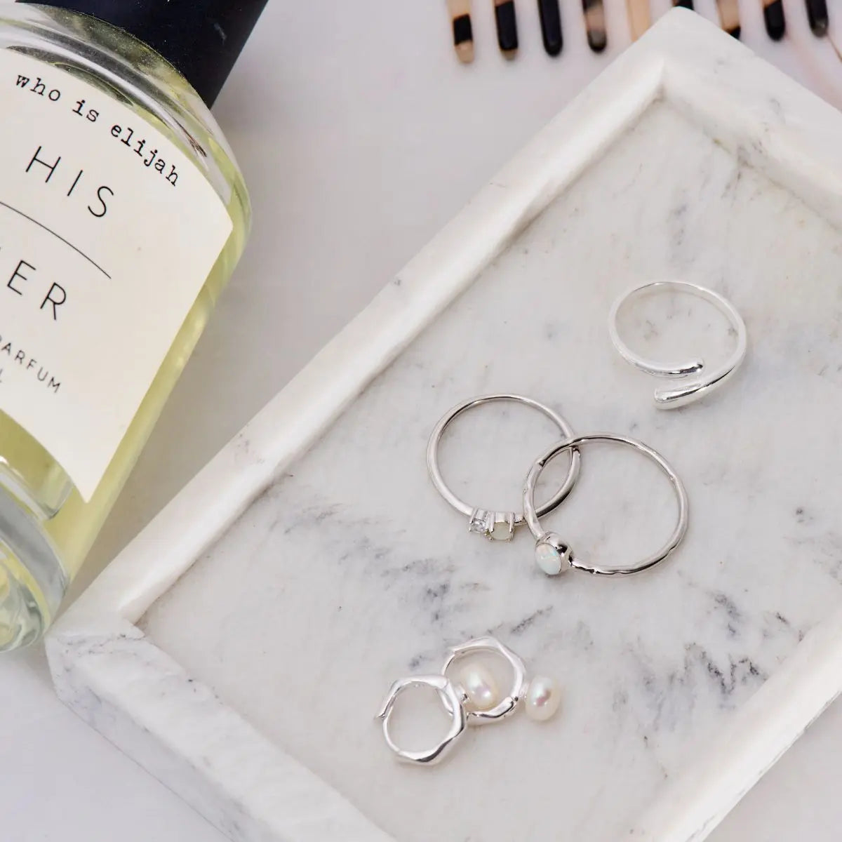 Silver hoop earrings with pearls on a marble surface next to a perfume bottle.