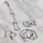 Silver jewelry set including rings and a necklace on a textured surface