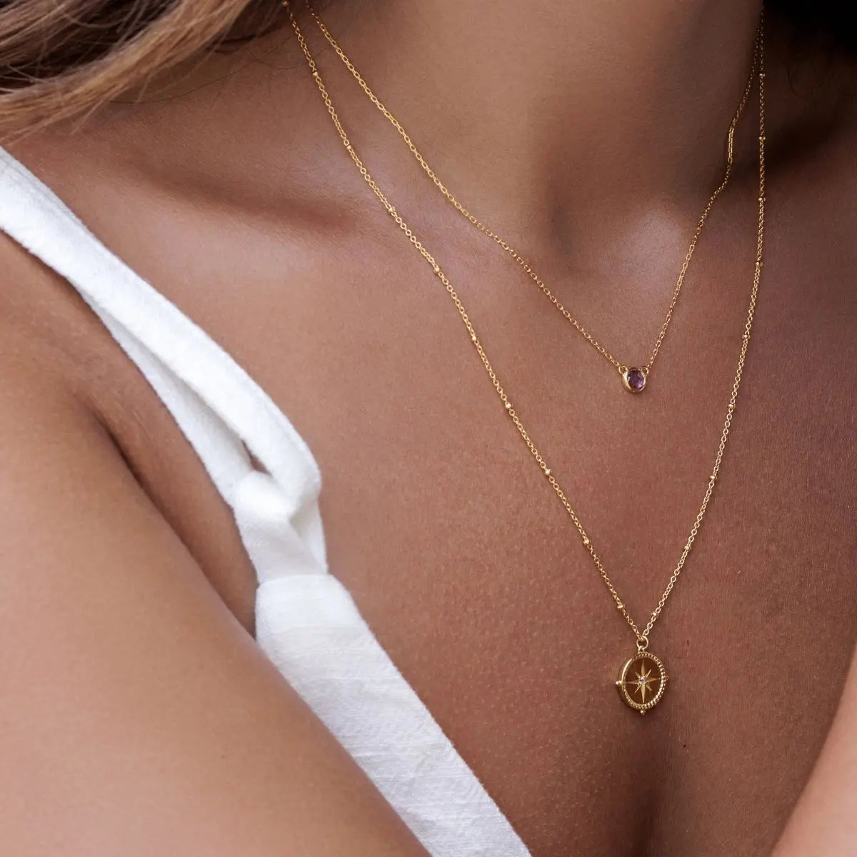Close-up of a person wearing a gold necklace with a compass pendant.