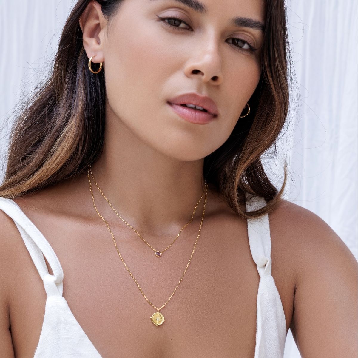 Woman wearing a gold necklace and earrings against a white background
