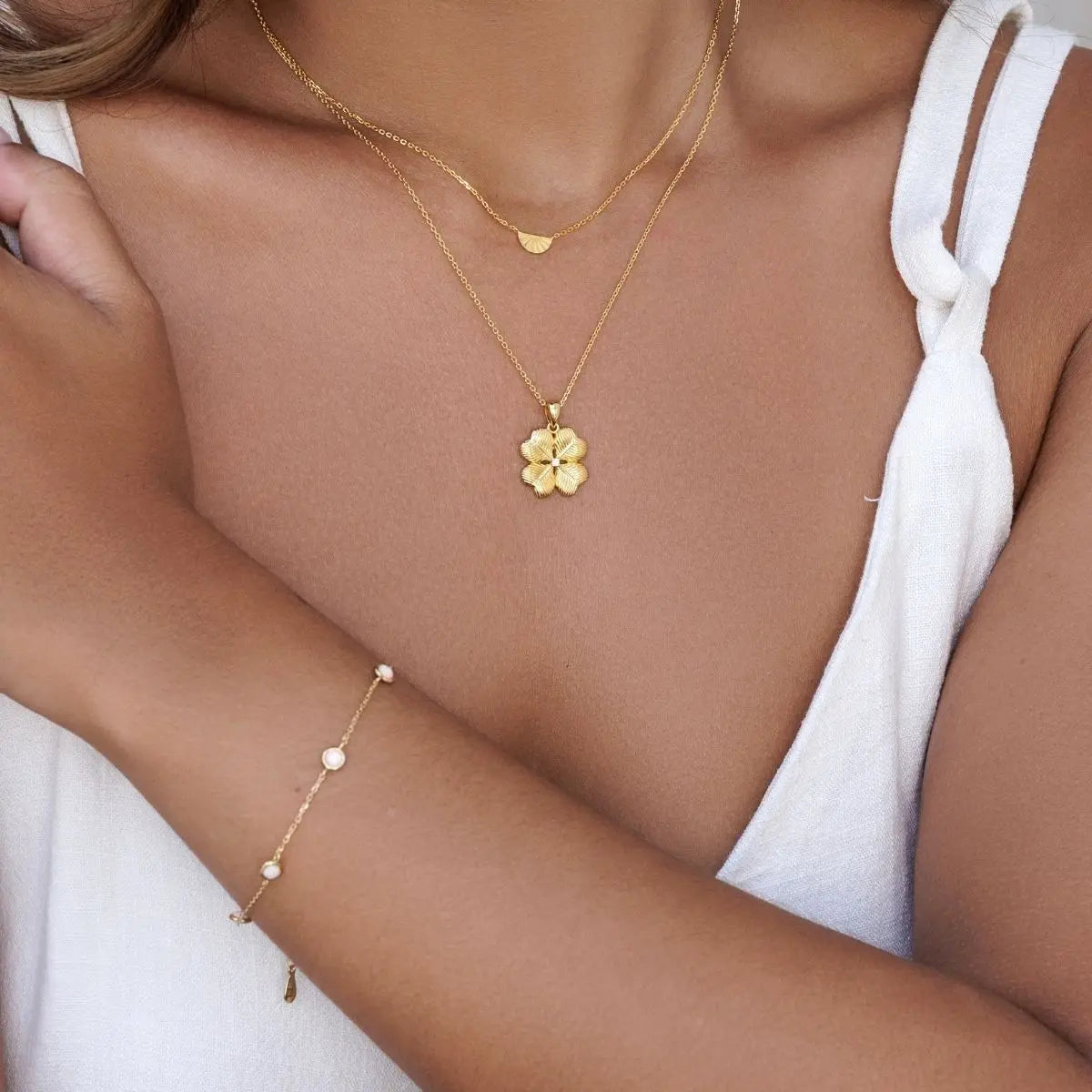 Gold necklace with a four leaf clover pendant and matching bracelet on a person wearing a white top.