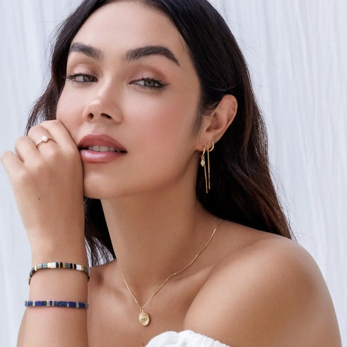 Woman wearing gold jewelry including earrings, necklace, and bracelets against a white background