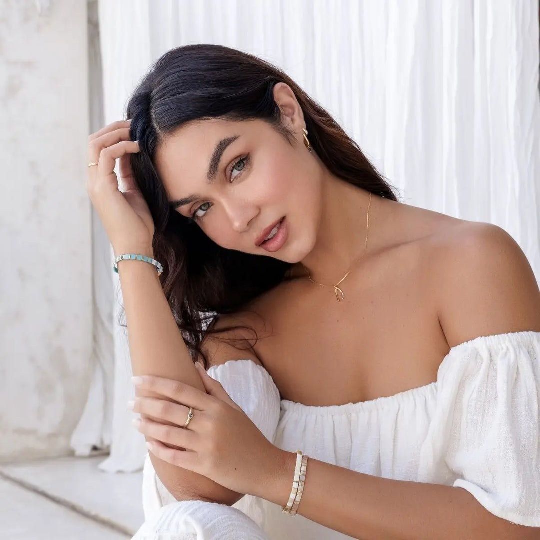 Woman in a white off-shoulder top sitting against a white curtain