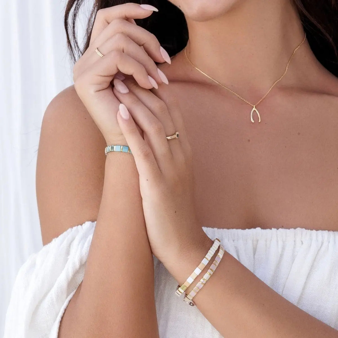Woman wearing a gold necklace, bracelet, and ring with a white background