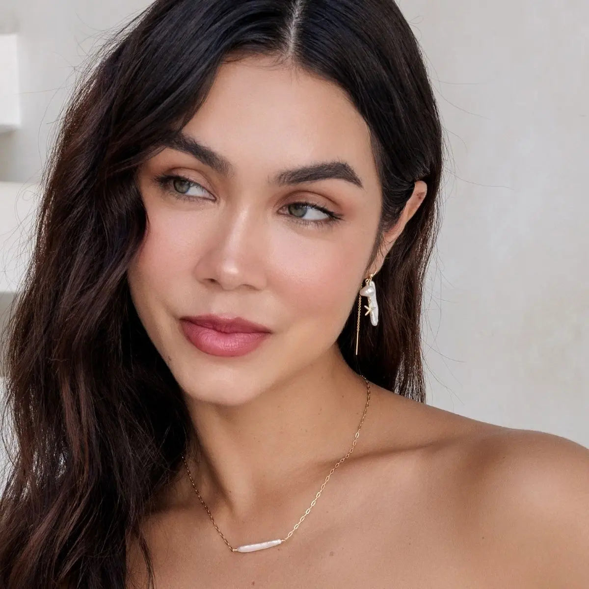 Woman wearing a necklace and earrings with a neutral background